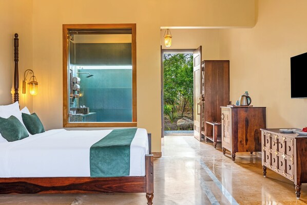 Habitación de hotel con cama, baño con puerta de vidrio, armario de madera y televisor en la pared.