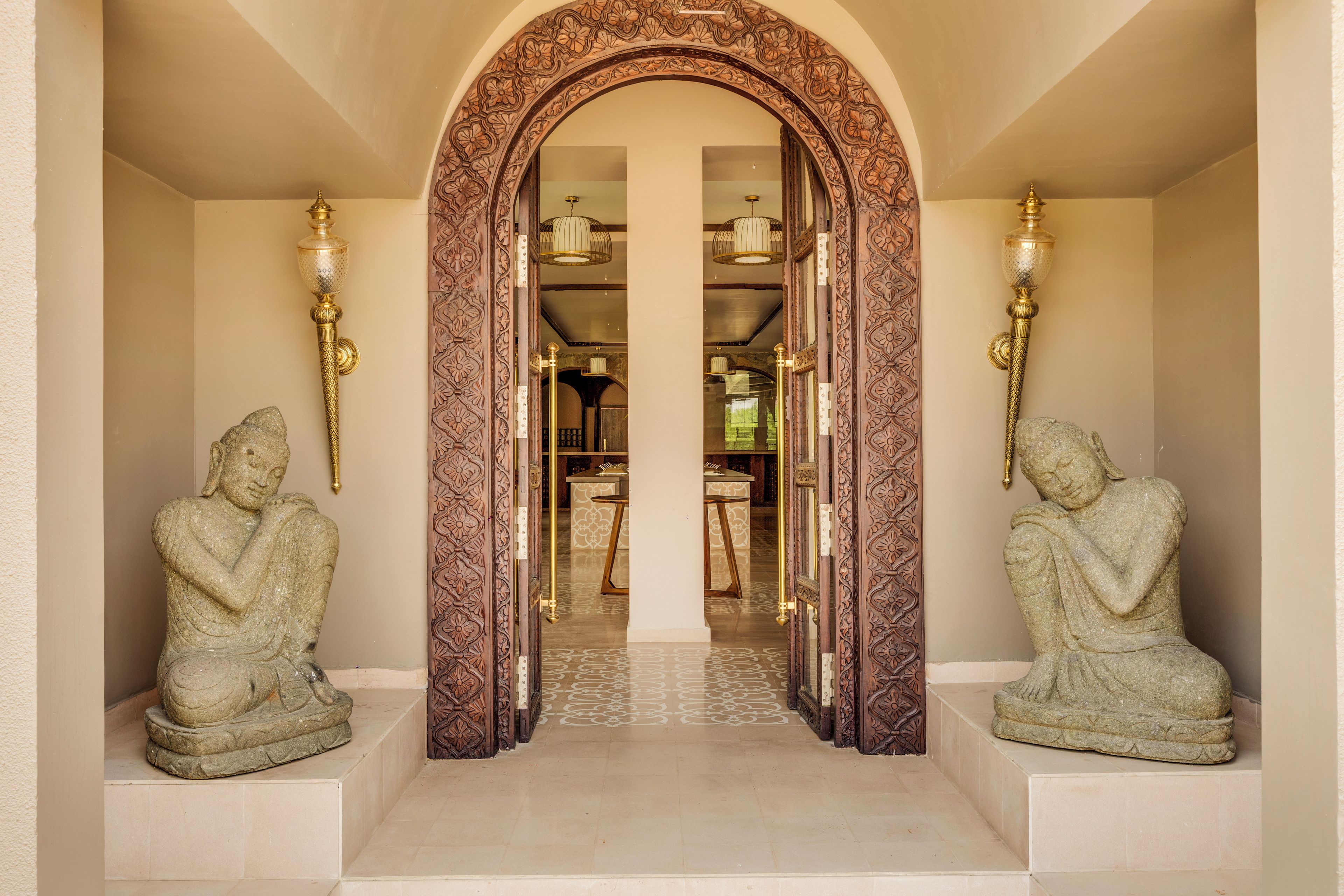 An entrance with an ornate wooden archway, two stone statues, and a glimpse of a dining area in the background.