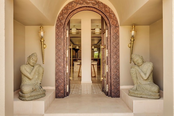 An entrance with an ornate wooden archway, two stone statues, and a glimpse of a dining area in the background.