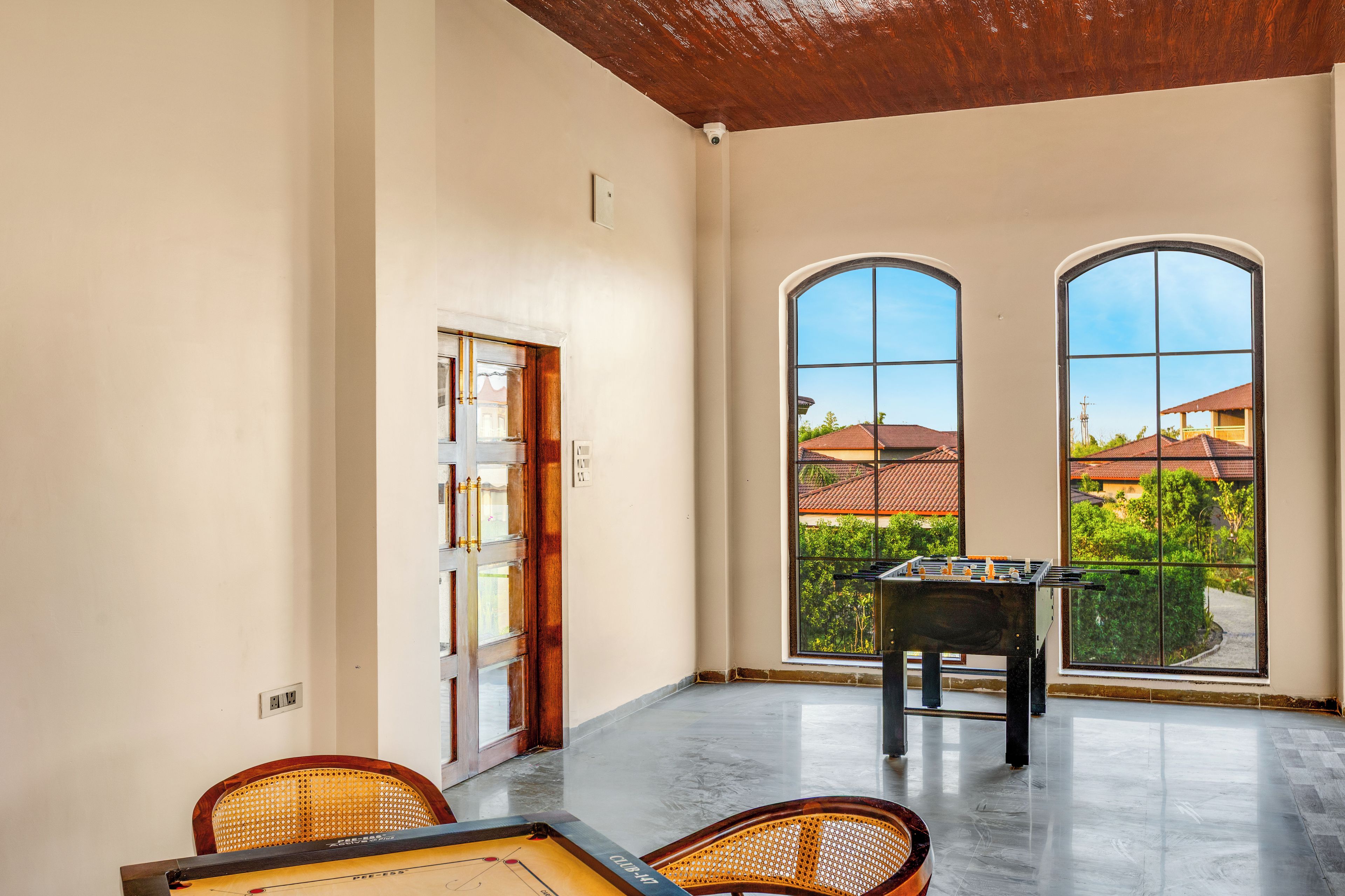 A spacious room with a foosball table, two large windows, and a door leading outside.