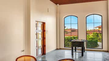 A spacious room with a foosball table, two large windows, and a door leading outside.