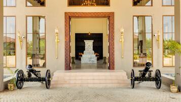 A building entrance with a marble staircase leading to a foyer, flanked by two large, ornate water wheels.