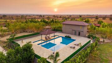 A pool area with a gazebo, lounge chairs, and a small building with a tiled roof.