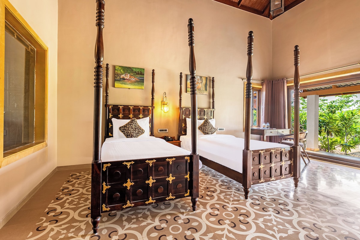 A four-poster bed with a dark finish and decorative gold accents, a large window with curtains, and a patterned floor.