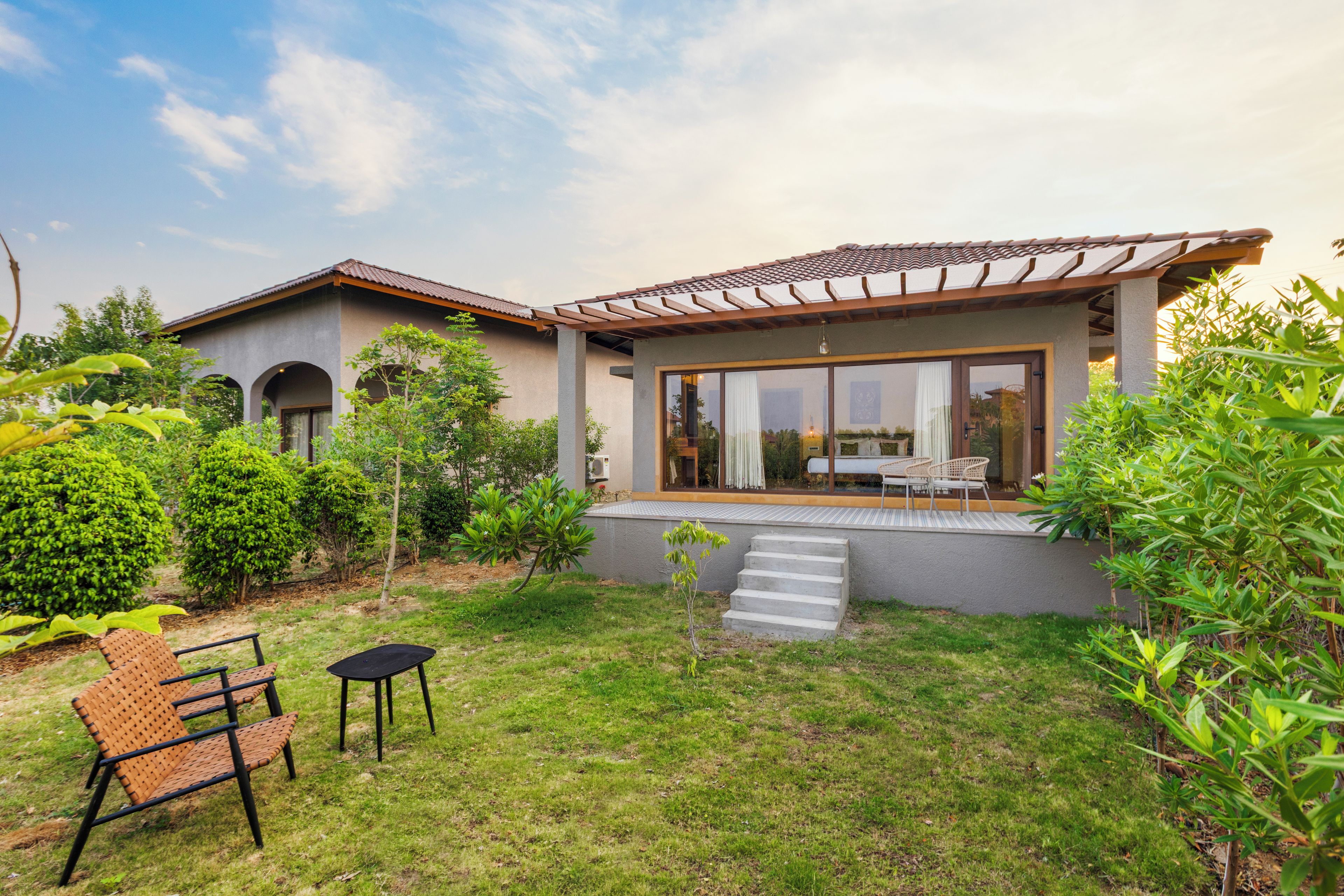 A modern house with a patio, a dining area with chairs, and a small garden.