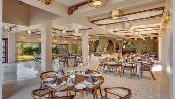 A spacious dining area with multiple tables and chairs, a central bar, and a view of the outdoors.