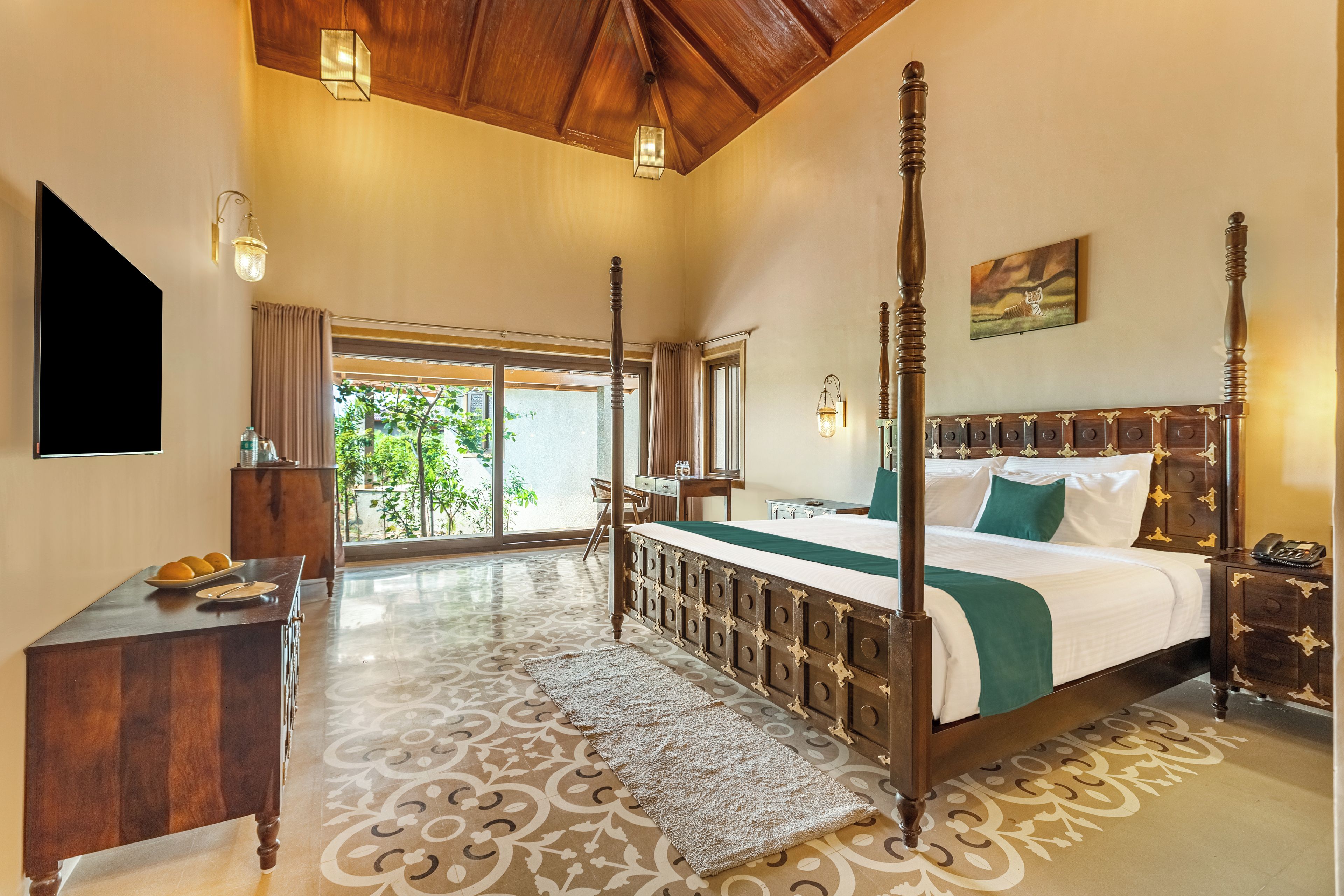 A spacious bedroom with a large bed, a desk, a chair, and a view of greenery outside.
