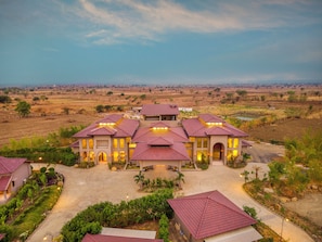 A large, multi-story building with a central courtyard, surrounded by open fields and a clear sky.