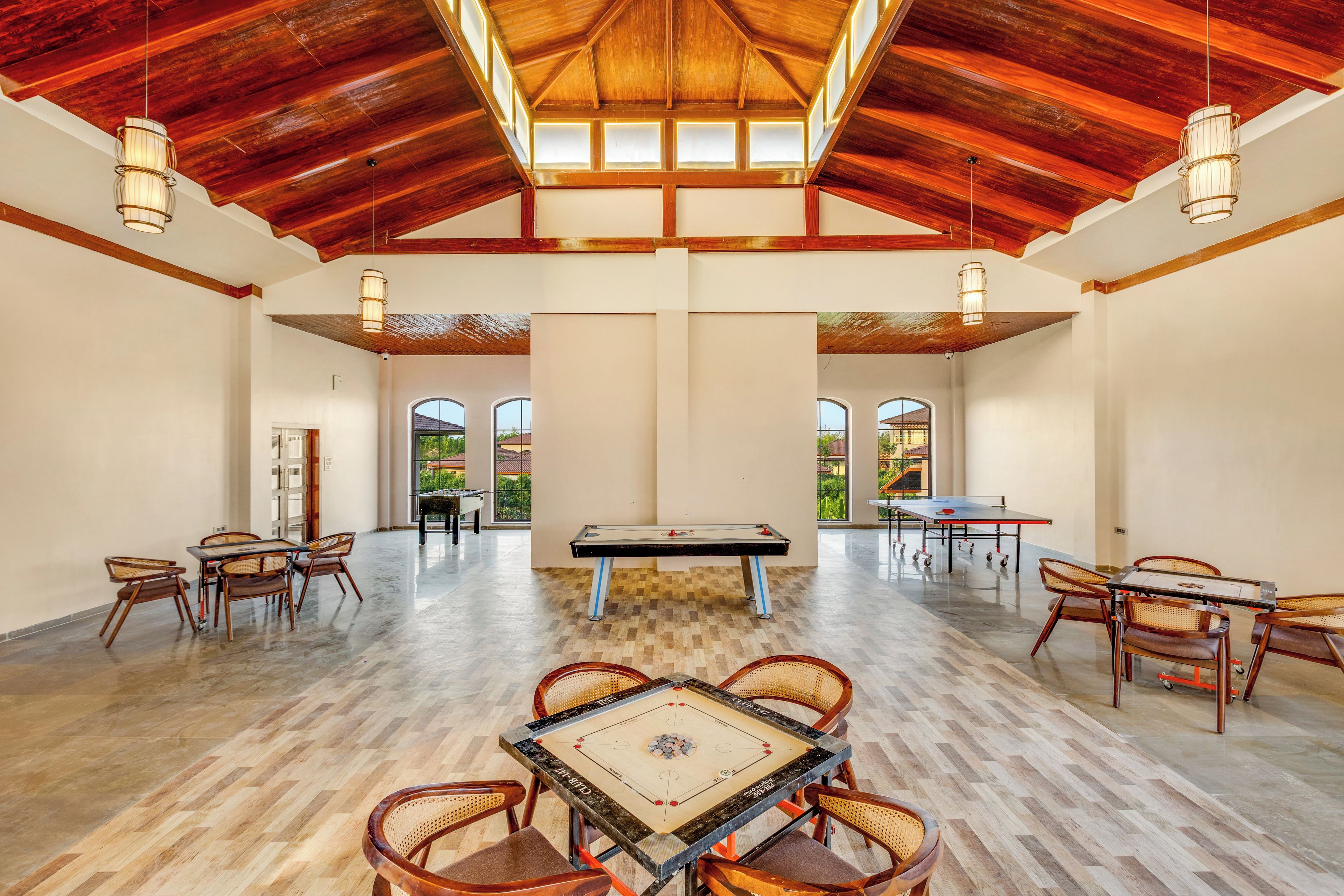 A spacious indoor area with a pool table, foosball table, and ping pong table, with high ceilings and natural light.