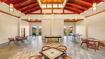 A spacious indoor area with a pool table, foosball table, and ping pong table, with high ceilings and natural light.
