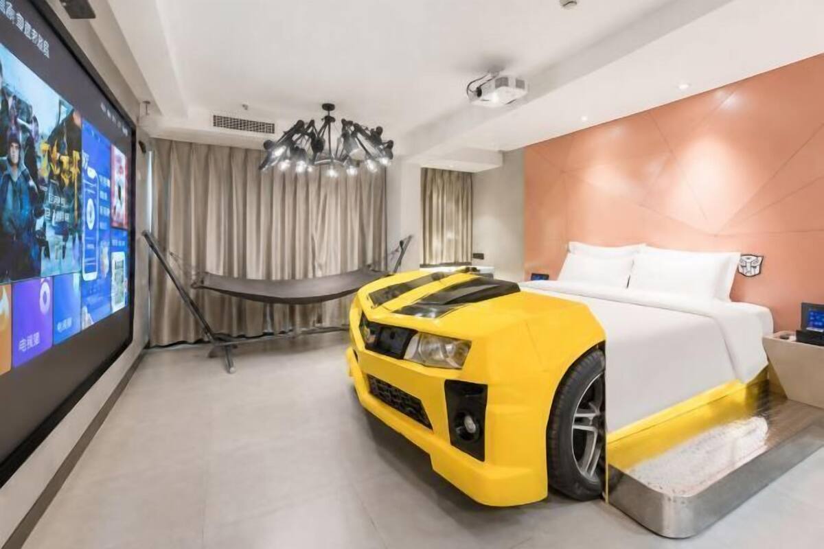 Una habitación de hotel moderna con una cama grande, una pantalla de televisión, una cama con forma de coche amarillo y un candelabro.