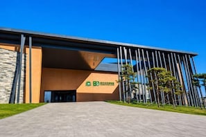 A modern building with a prominent entrance, a stone facade, and a green sign with white text.