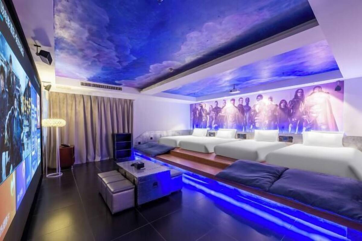 Un moderno cuarto de spa con un mural en el techo, un televisor de pared grande y una zona de estar con camilla de masaje.