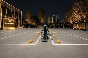 A nighttime parking area with electric vehicle charging stations, a building with illuminated signage, and trees lining the background.