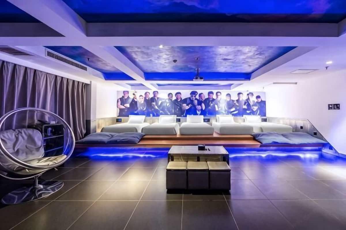 Una sala de estar moderna con un amplio espacio para sentarse, un sillón colgante y una pantalla montada en la pared que muestra a un grupo de personas.