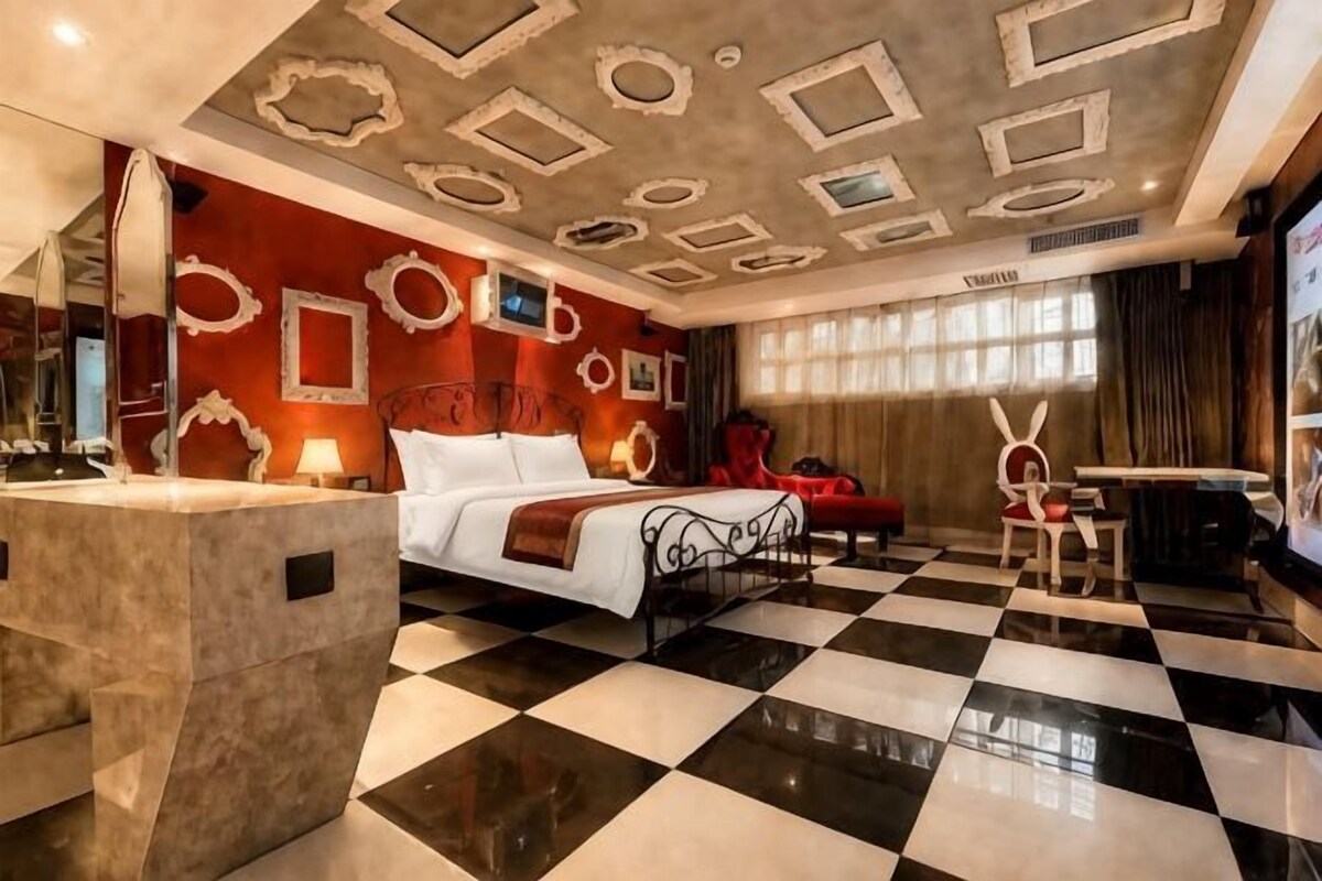 A hotel room with a checkered floor, a bed, a desk, and a mirror.