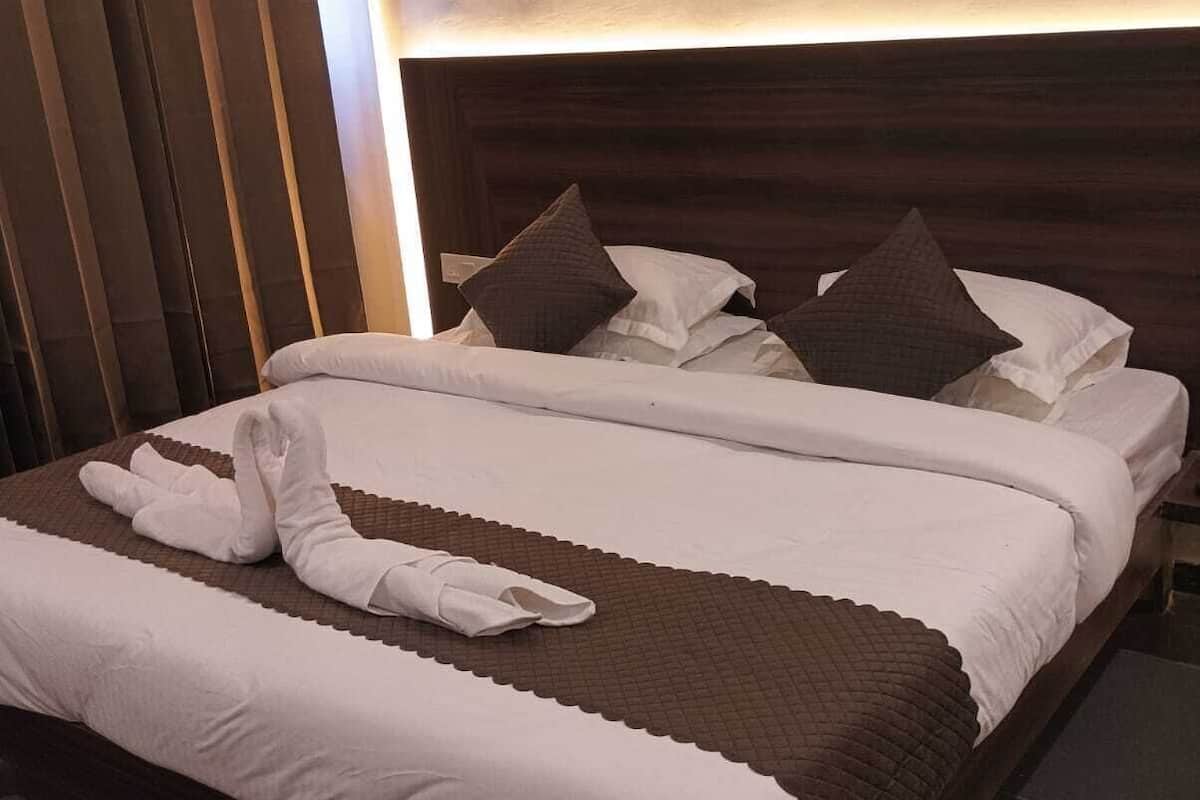 A neatly made bed with white linens and brown pillows, a wooden headboard, and a dark curtain.