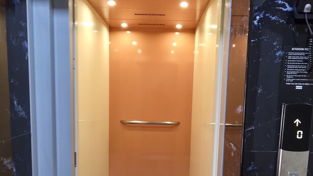 Un ascensor con barandilla metálica, un panel de control con una flecha hacia arriba y un cartel con instrucciones.