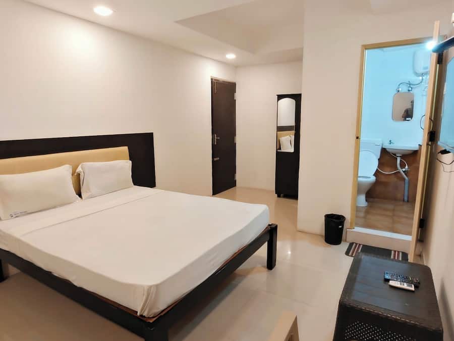 Un dormitorio con cama, escritorio, silla, espejo y puerta que da a un baño.