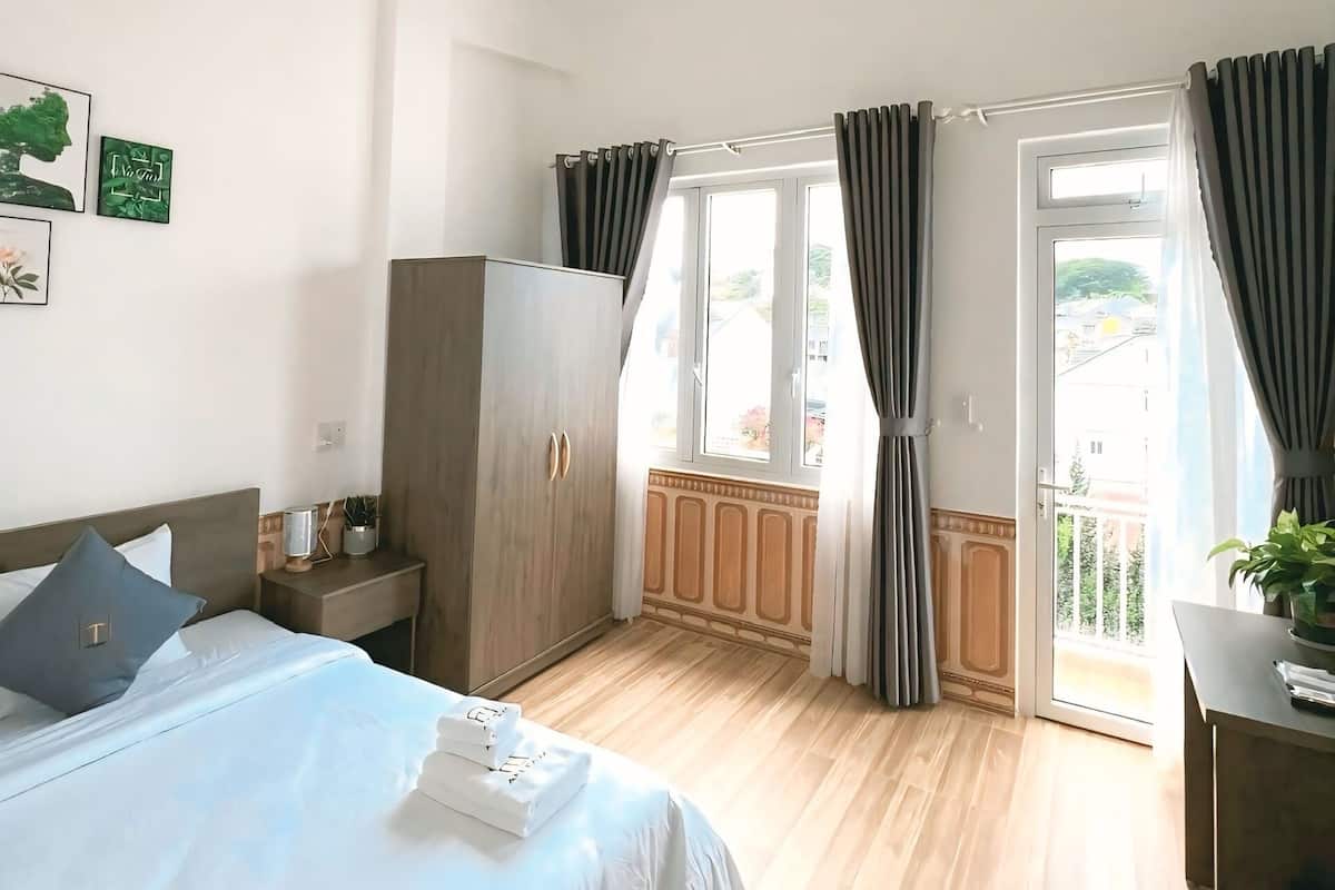 Quarto com cama, guarda-roupa, mesa de cabeceira com luminária, janela com cortinas e vista para o exterior.