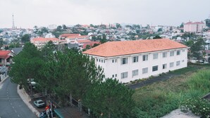 Un edificio blanco con techo rojo, rodeado de árboles y una calle.