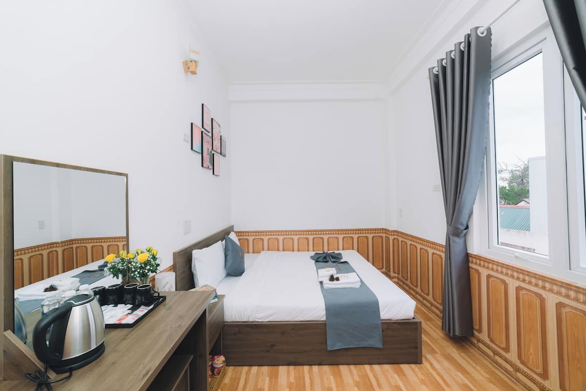 Quarto de hotel com cama, mesa de cabeceira, espelho e janela com cortinas.