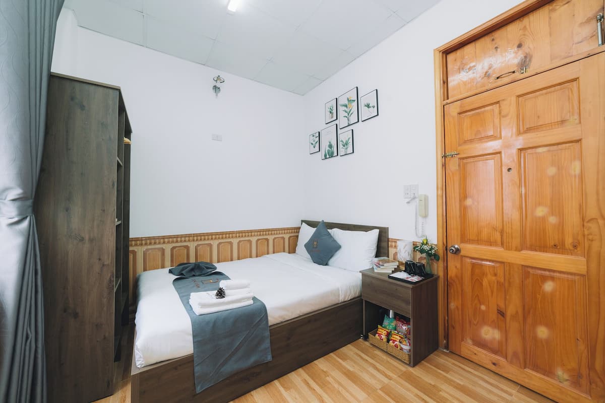 Quarto com cama de madeira, mesa de cabeceira, guarda-roupa e porta.