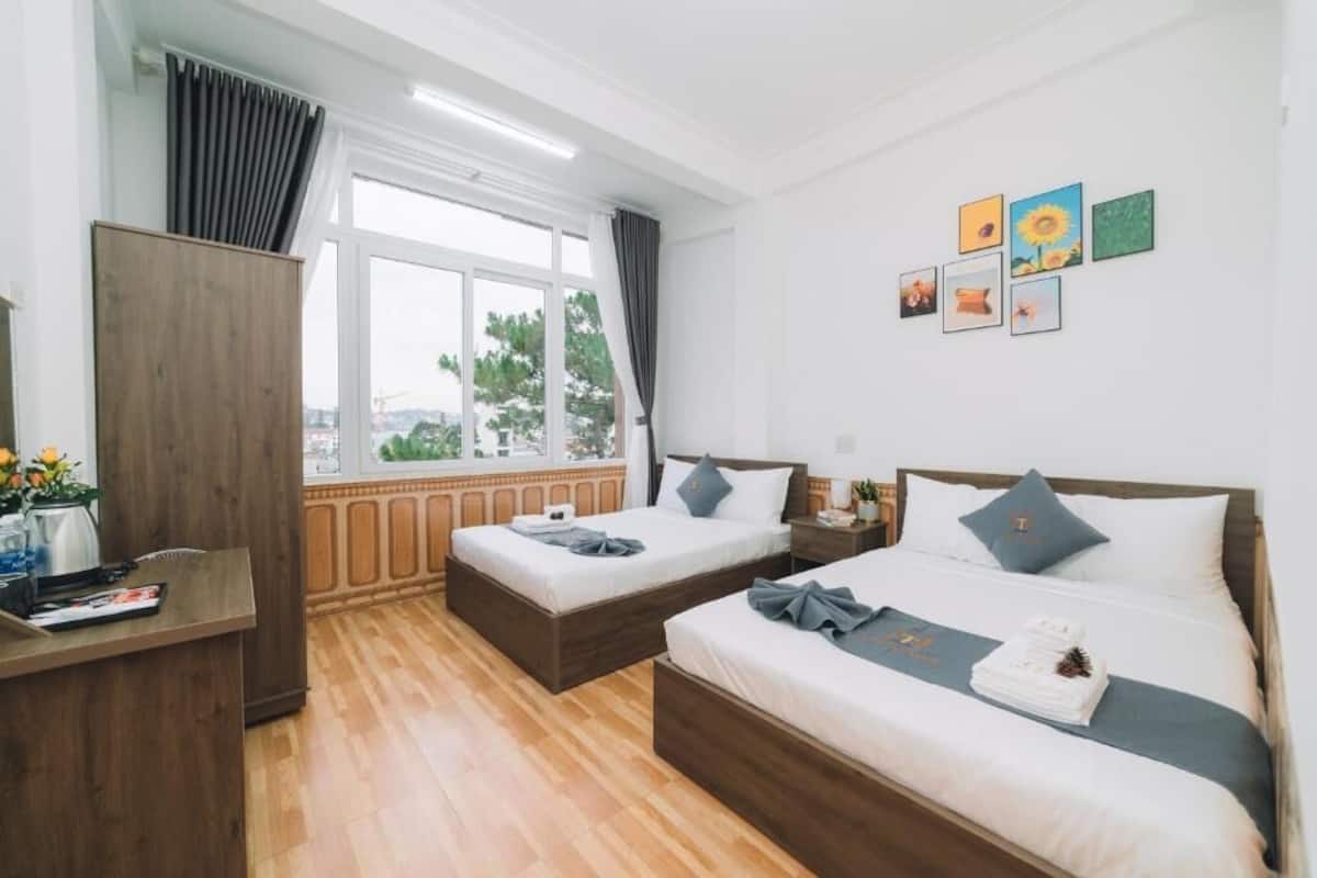 Quarto de hotel com duas camas, uma escrivaninha de madeira, uma janela com cortinas e obras de arte na parede.