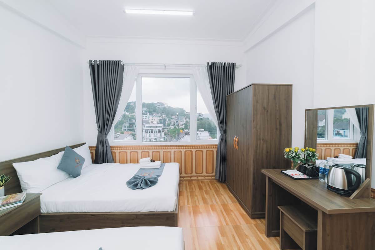 Quarto de hotel com cama, escrivaninha, guarda-roupa e janela com vista para a cidade.