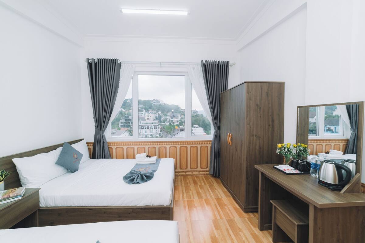 A hotel room with a bed, a desk, a wardrobe, and a window with a city view.