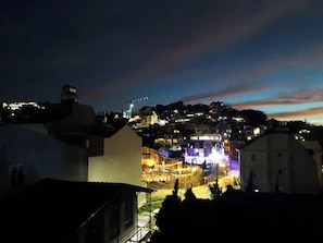 Vista nocturna de un pueblo con edificios iluminados y una colina al fondo.