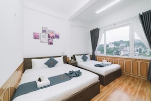 Quarto de hotel com duas camas, uma janela grande com cortinas, vista para a cidade e uma parede com quadros.