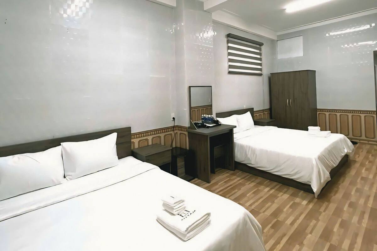 Quarto de hotel com duas camas, uma escrivaninha, um guarda-roupa e um espelho.