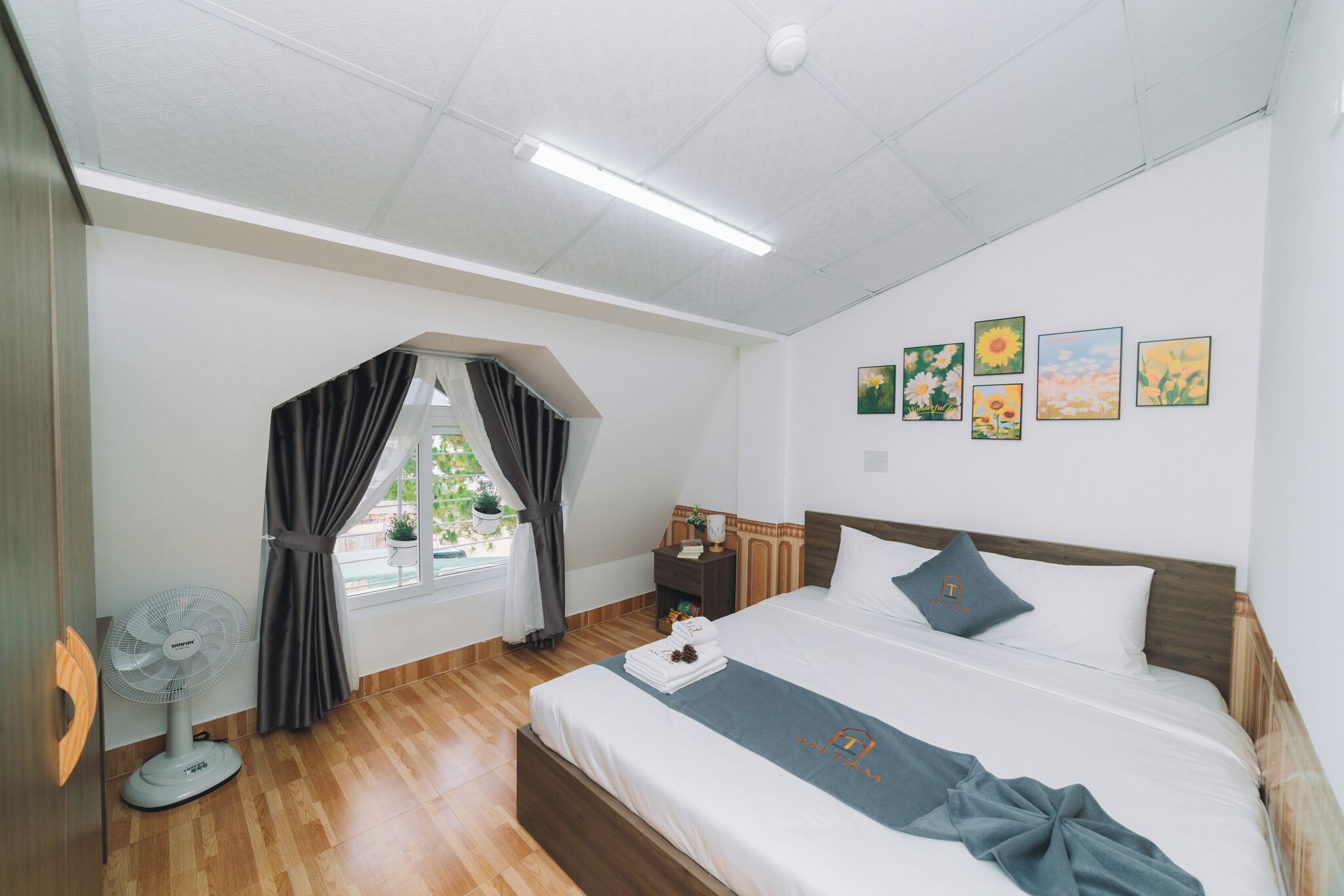 Ein Hotelzimmer mit Bett, Nachttisch, Vorhängen am Fenster und Wandbildern.