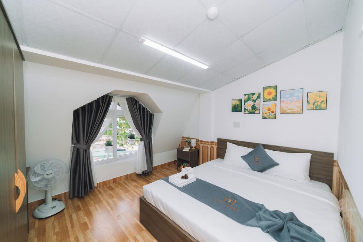 Quarto de hotel com cama, mesa de cabeceira, cortinas e uma obra de arte na parede.