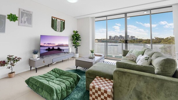 Un soggiorno moderno con una grande TV, mobili verdi, un balcone con vista sulla città e una pianta.