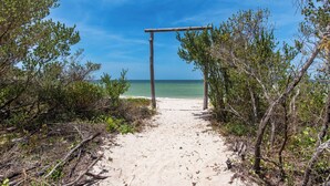 A sandy beach path leading to a wooden archway with a clear view of the ocean.