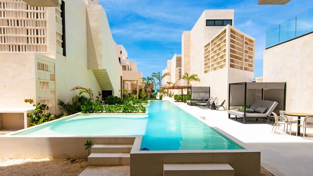 A swimming pool with steps leading into it, surrounded by modern buildings and outdoor seating.