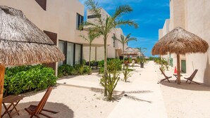 A resort with thatched umbrellas, palm trees, and a sandy walkway.