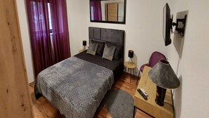 Ein Schlafzimmer mit Bett, Deckenventilator, Klimaanlage, Spiegel, Lampe und einem kleinen Tisch.