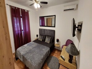 Ein Schlafzimmer mit Bett, Deckenventilator, Klimaanlage, Spiegel, Lampe und einem kleinen Tisch.
