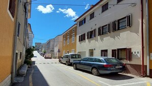 Eine enge Straße mit parkenden Autos, Häusern an beiden Seiten und blauem Himmel.