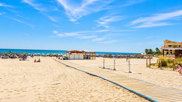 Een strand met een houten looppad, parasols en mensen op het strand.