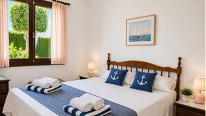 Een opgemaakt bed met blauw-wit beddengoed, een houten hoofdbord en twee kussens met anker afbeeldingen.
