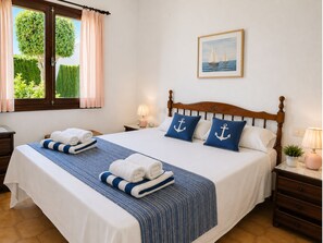 Ein ordentlich bezogenes Bett mit blau-weißer Bettwäsche, einem Holz-Kopfteil und zwei Kissen mit Anker-Motiven.