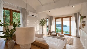 Een slaapkamer met een groot bed, een houten nachtkastje, een potplant en uitzicht op zee.