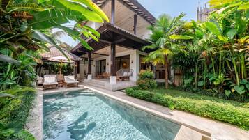 A poolside area with lounge chairs, a covered seating area, and lush tropical vegetation.