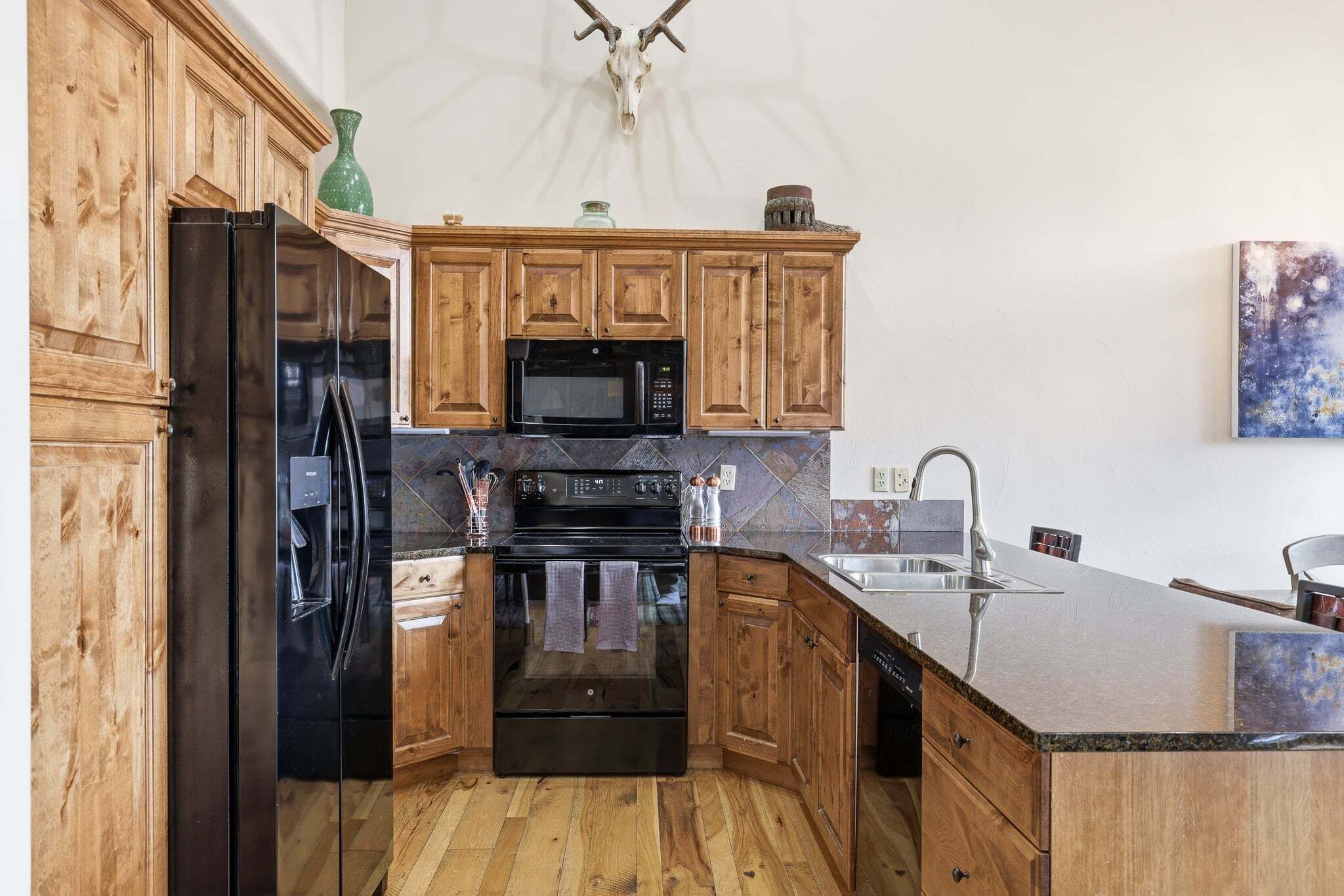 A kitchen with wooden cabinets, a black refrigerator, a microwave, an oven, and a sink.