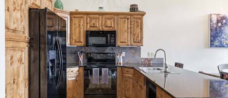 A kitchen with wooden cabinets, a black refrigerator, a microwave, an oven, and a sink.