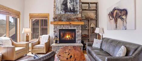 A cozy living room with a stone fireplace, leather furniture, and artwork on the walls.
